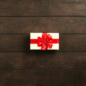 Top view of a gift box with red ribbon on a dark wooden background, offering ample copyspace.